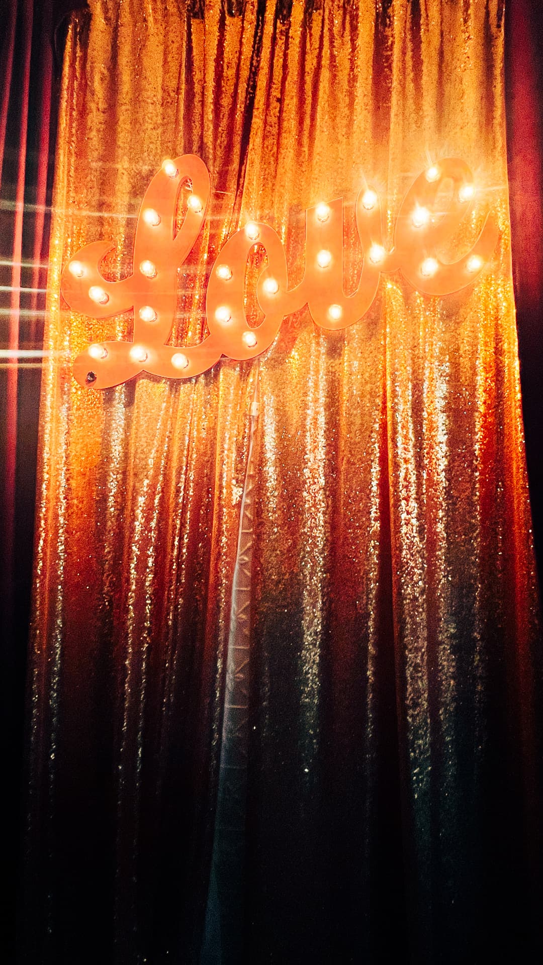Glowing Love marquee sign against a gold curtain