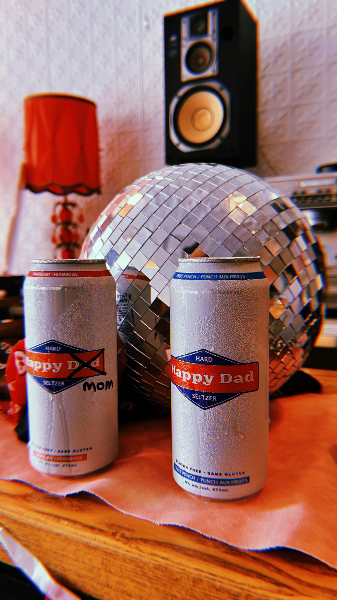 Two Happy Dad seltzer cans in front of a disco ball and speaker